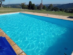 A clear blue swimming pool with a view of the surrounding landscape. - Country house for rent (São Roque)