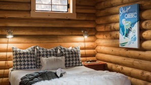 A log cabin bedroom with a wooden bed, a window, a wall-mounted lamp, and a poster. - Outpost: Alpine Cottage Studio (Jackson)
