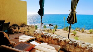 Un muro di pietra con vista sull'oceano, sedute all'aperto con cuscini e ombrelloni.