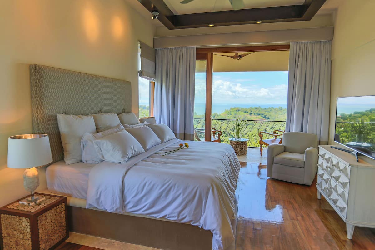 Une chambre avec un grand lit, une télévision, un fauteuil et un balcon avec vue.