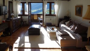 Un salon chaleureux avec un canapé, une table basse et une vue sur un paysage montagneux, visible à travers de grandes fenêtres.