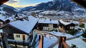 Un village enneigé, avec des bâtiments traditionnels et une chaîne de montagnes en arrière-plan.