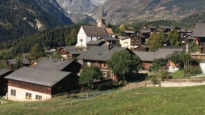 Un village de montagne aux maisons traditionnelles en bois, avec une église, et une vue dégagée sur les sommets enneigés qui se dressent à l'arrière-plan.
