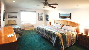 Une chambre d’hôtel avec deux lits, un ventilateur de plafond, une fenêtre avec des rideaux et des tableaux encadrés accrochés aux murs.