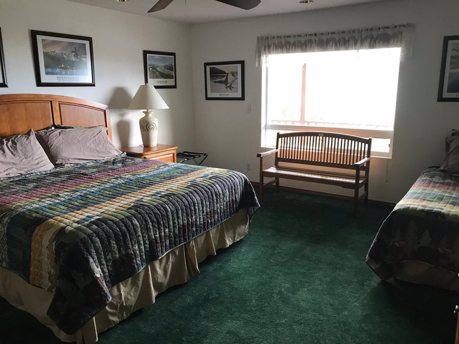 Quarto com uma cama grande, um banquinho de madeira, uma mesa de cabeceira e uma janela com vista.