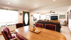 Un coin repas avec une table en bois, des chaises à l’assise rembourrée de couleur rouge, une porte verte et un téléviseur en arrière-plan.