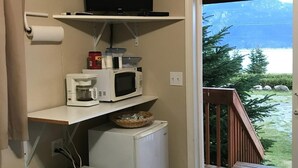 A compact kitchenette with a microwave, coffee maker, and a small refrigerator. A television is mounted above the microwave. - Cabin 1 Lynn View Lodge (Haines)
