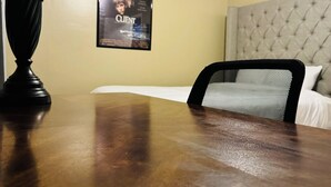 A hotel room with a wooden table, a ceiling fan, a bed with a tufted headboard, and a poster on the wall. - NC Music Factory Ranch Getaway (Charlotte)
