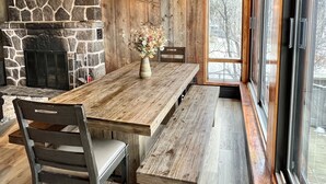 Ein Essbereich mit einem langen Holztisch, einem Steinofen und großen Fenstern.