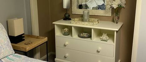 A bedroom with a bed, a dresser with drawers, a mirror, a nightstand, and a vase with flowers.