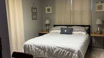 A neatly arranged bedroom with a bed, two bedside tables with lamps, a chair, and a desk.