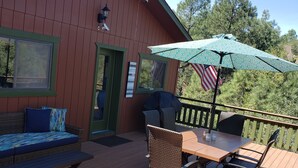 A wooden deck with a table and chairs, an American flag, and a covered area with an umbrella. - Interior Designer Farm-Style Accommodations in the Pines (Prescott)