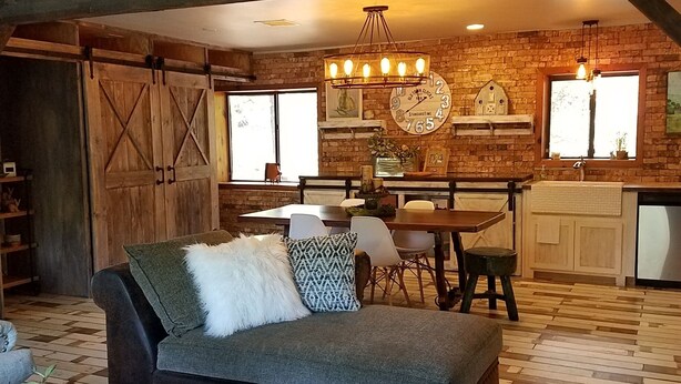A cozy living room with a sofa, a coffee table, and a dining area with a table and chairs. There is a kitchen area with a refrigerator and a window. - Interior Designer Farm-Style Accommodations in the Pines (Prescott)