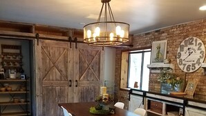 A rustic kitchen with a wooden table, chairs, a chandelier, and a vintage clock. - Interior Designer Farm-Style Accommodations in the Pines (Prescott)