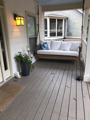 A porch with a swing seat, a potted plant, and a door with a doormat. - Pretty little Cottage (Oxford)