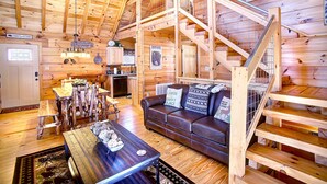 Ein Interieur einer Holzhütte mit einer Holztreppe, einem Essbereich, einem Wohnzimmer mit einer Couch und einer Küchenzeile.
