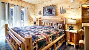 Ein Schlafzimmer in einer Blockhütte mit einem großen Bett, einem Holzkopfstück und einem Deckenventilator.