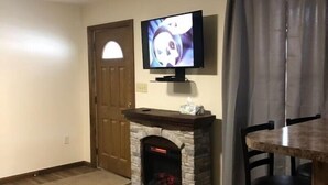 Ein Wohnzimmer mit Kamin aus Stein, einem an der Wand montierten Fernseher, einer Holztür und einem Essbereich mit Tisch und Stühlen.