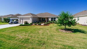 A residential house with a garage, a driveway, and a small tree in the front yard. - Ruhe Haus in Collier. 3/2, FREE golf, 4-seat cart, RESIDENT passes, pets (The Villages)