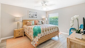 A bedroom with a bed, bedside tables, a ceiling fan, a window with blinds, and a desk with a plant. - Ruhe Haus in Collier. 3/2, FREE golf, 4-seat cart, RESIDENT passes, pets (The Villages)
