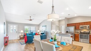 A spacious living area with a dining table, blue sofa, and a kitchen with modern appliances. - Ruhe Haus in Collier. 3/2, FREE golf, 4-seat cart, RESIDENT passes, pets (The Villages)