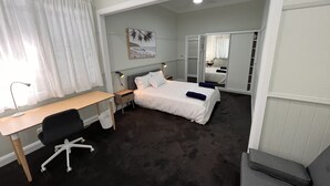 Hotellihuoneessa on työpöytä, tuoli, kaksi sänkyä, peili ja taulu seinällä.