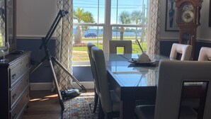 Een eetruimte met een glazen tafel, stoelen, een kroonluchter, een klok en uitzicht op het landschap.