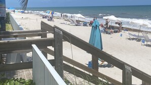 Een strand met houten leuningen, ligstoelen, parasols en mensen die van de zee genieten.