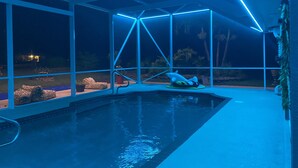 Een zwembad met een drijvend dolfijnbeeld, omgeven door een glazen structuur met blauwe verlichting.