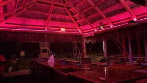 Een terras met een rieten dak, rode verlichting en een pooltafel.