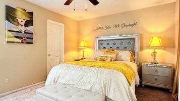 A bedroom with a bed, two bedside tables with lamps, a ceiling fan, a door, and a painting on the wall.