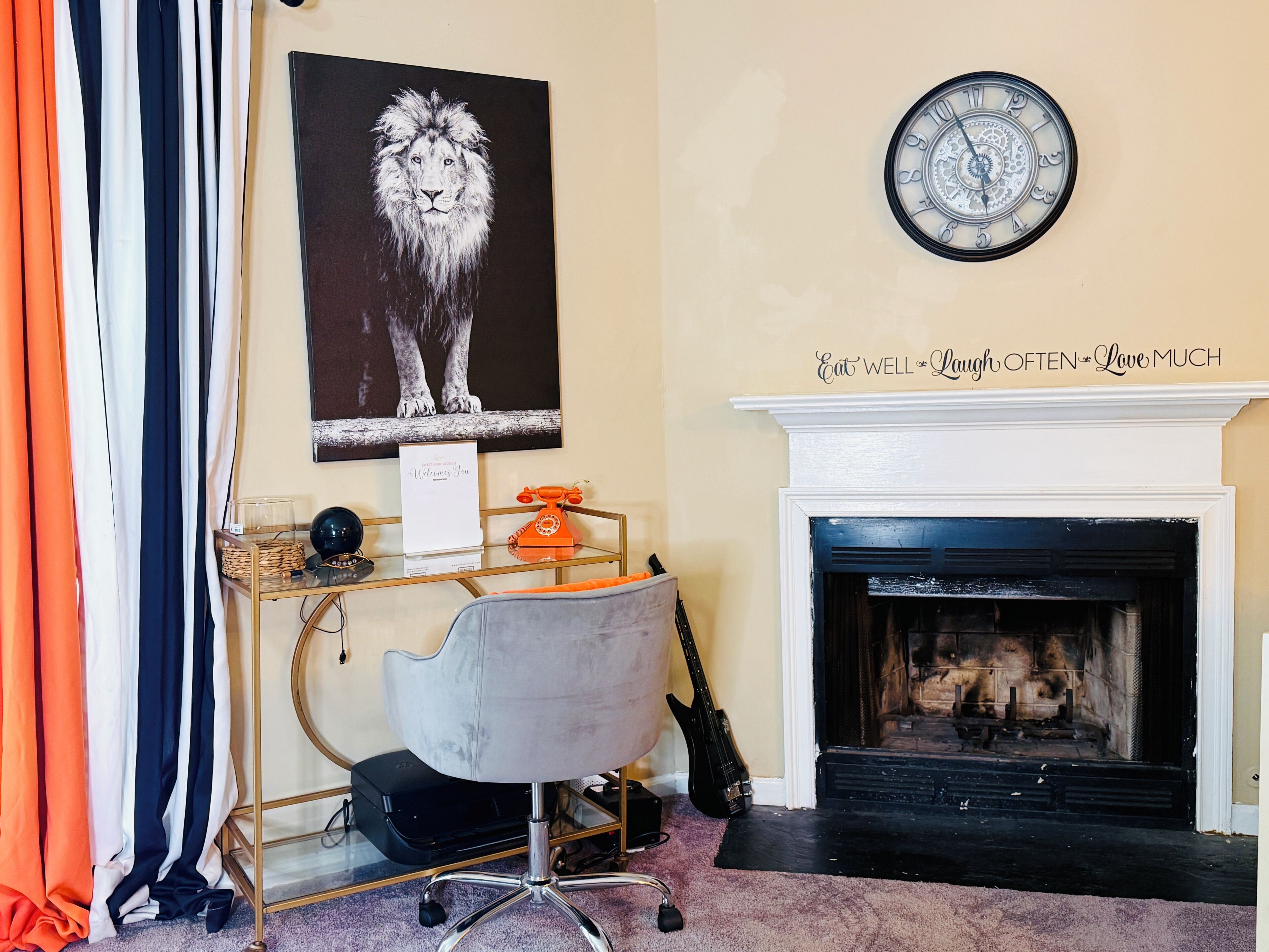 A room with a fireplace, a clock, a desk with a telephone, a chair, and a framed picture of a lion.