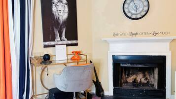 A room with a fireplace, a clock, a desk with a telephone, a chair, and a framed picture of a lion.