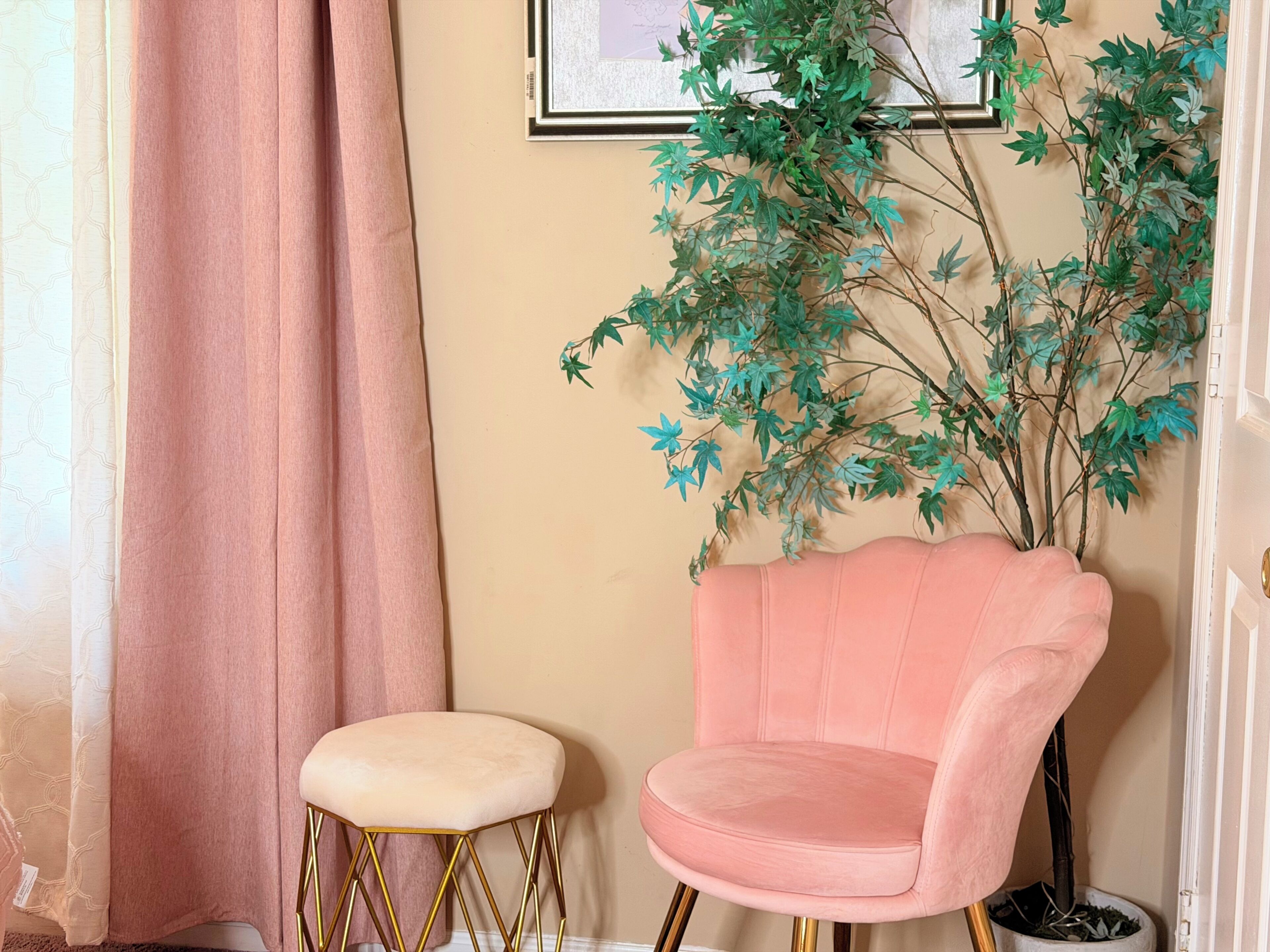 A room with a pink chair, a small stool, and a wall-mounted artificial plant.