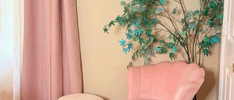 A room with a pink chair, a small stool, and a wall-mounted artificial plant.