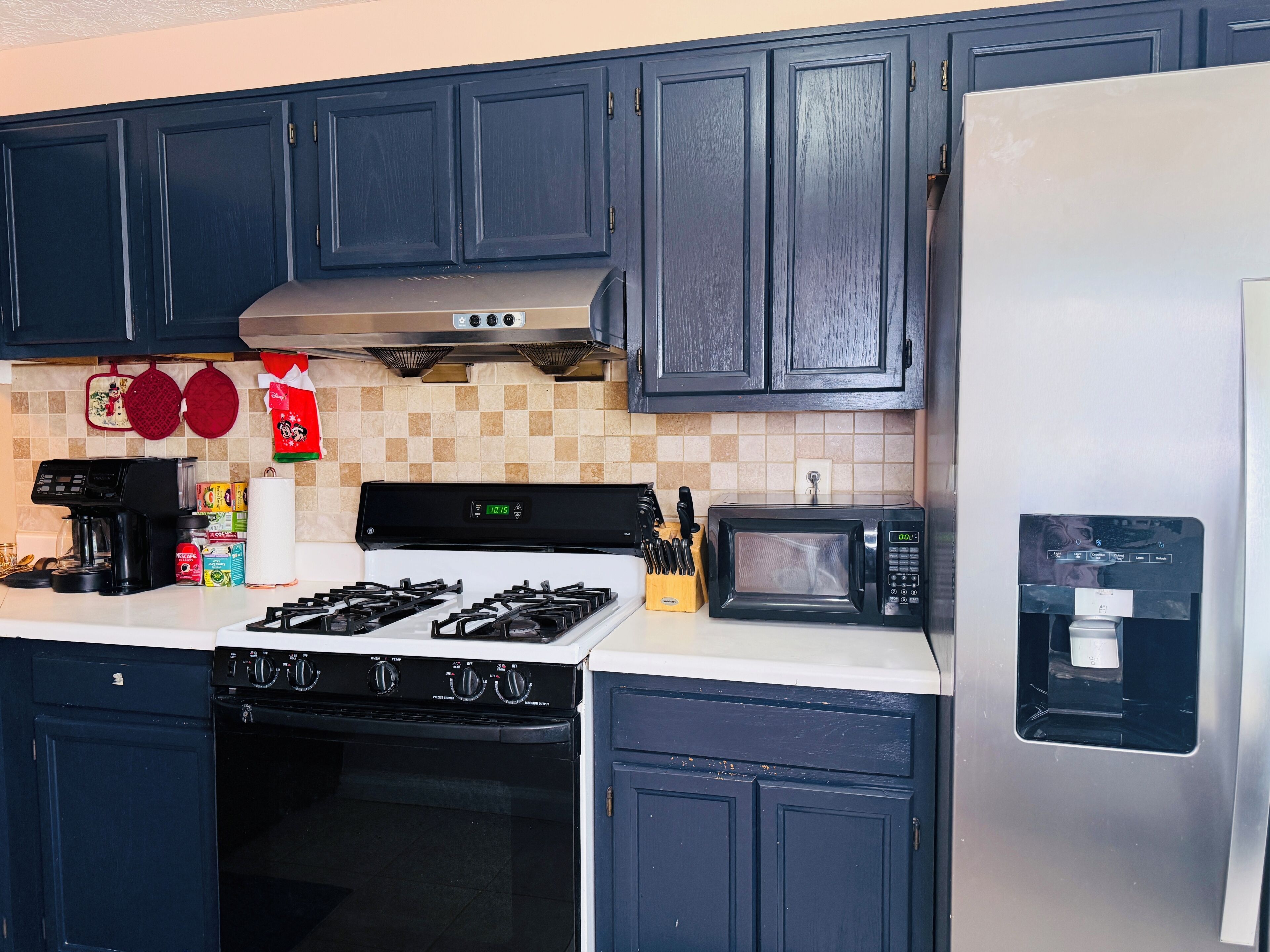 A kitchen with dark cabinets, a gas stove, a microwave, and a water dispenser.