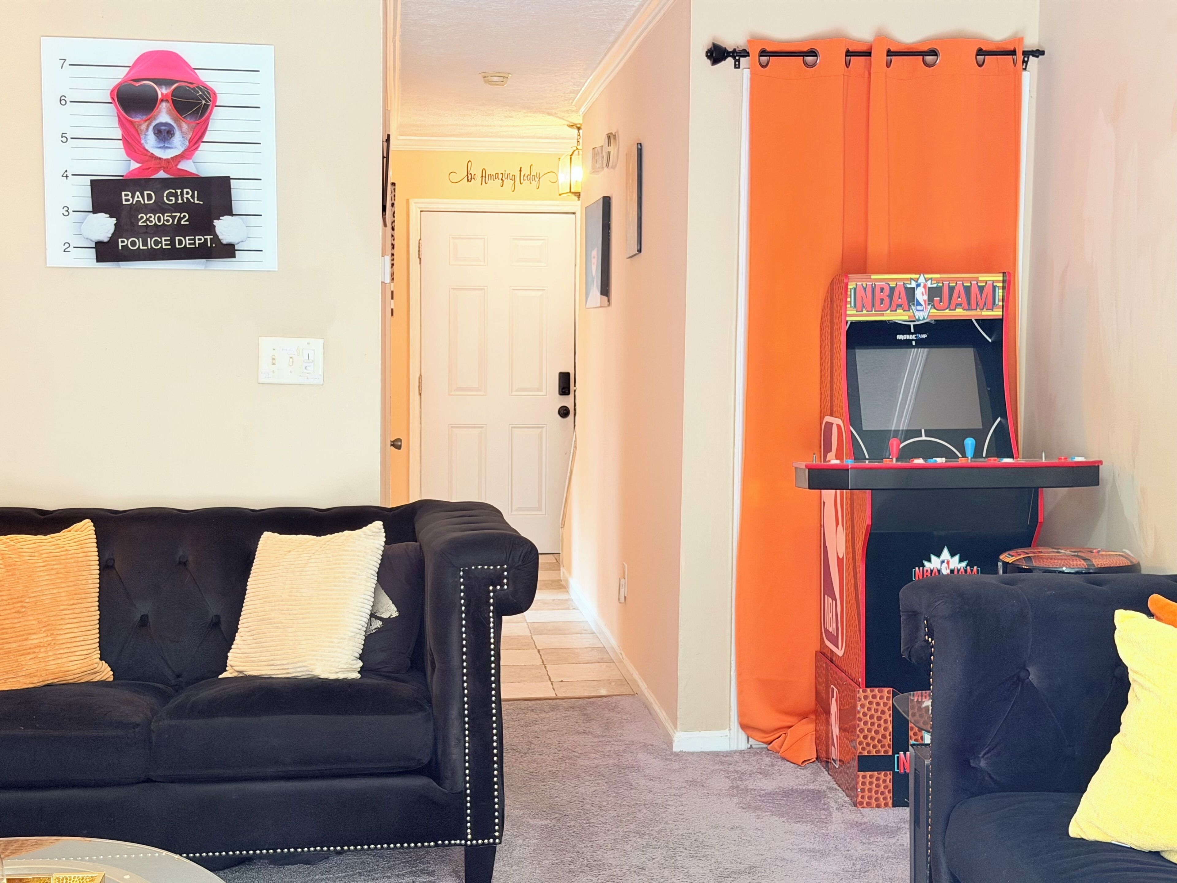 A living room with a black sofa, a small table, and an orange curtain.