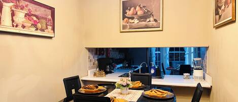 Un comedor con una mesa dispuesta para cuatro personas, una araña y cuadros en las paredes.