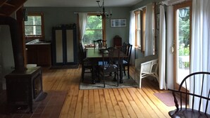 Een eetgedeelte met een houten tafel en stoelen, een kroonluchter en uitzicht op de omgeving door grote ramen.