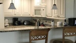 A kitchen with white cabinets, a microwave, a coffee maker, and two bar stools. - Chateaux #406  Charming Beachfront Retreat with spectacular views! (Indian Shores)