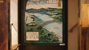 Una habitación japonesa tradicional con suelo de tatami, puerta corredera shoji y vista a un cerezo en flor.