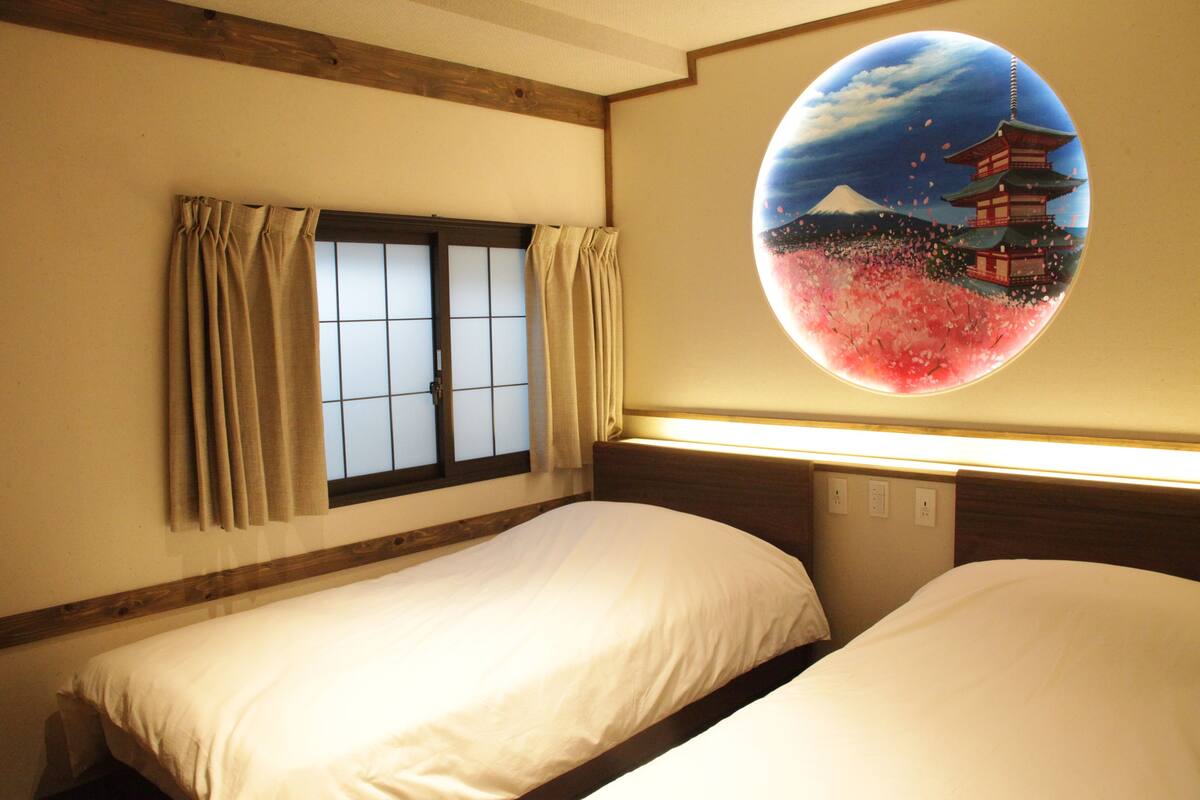 A hotel room with two beds, a shoji screen, and a large circular painting of a pagoda.