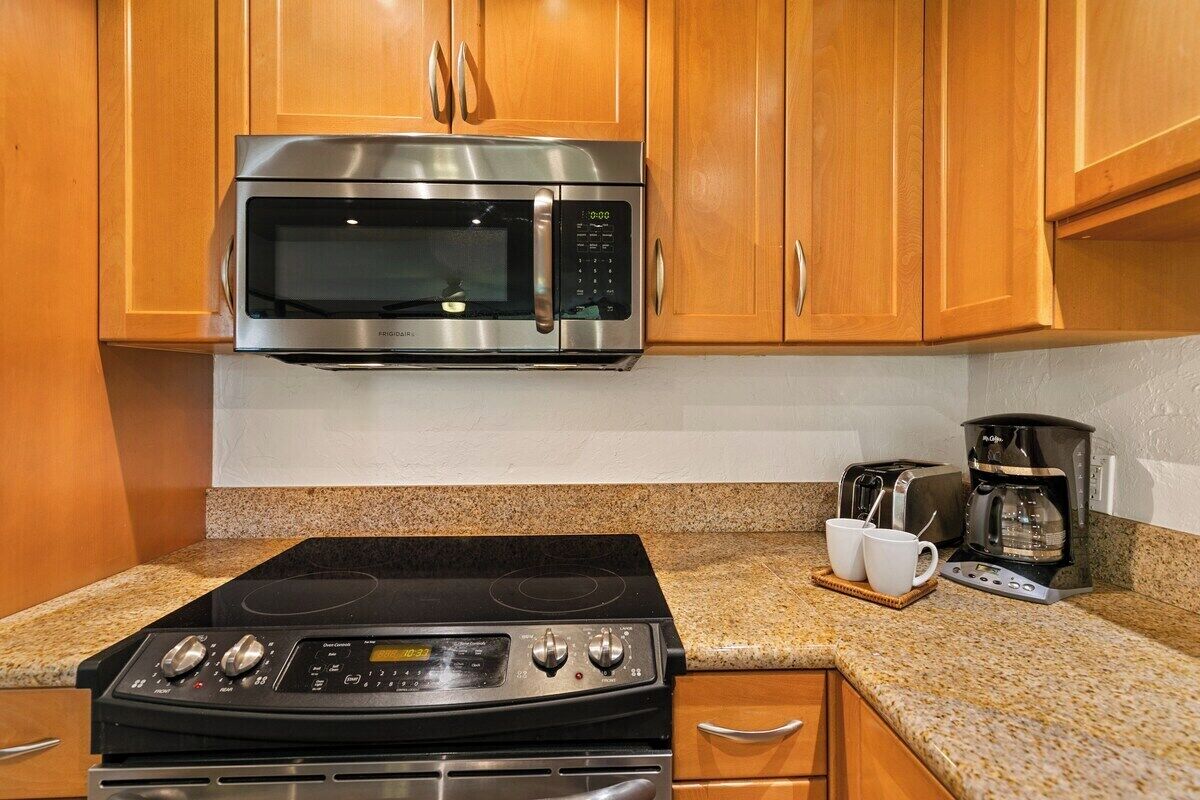 A kitchen with wooden cabinets, a stainless steel microwave, a black stovetop, and a coffee maker.