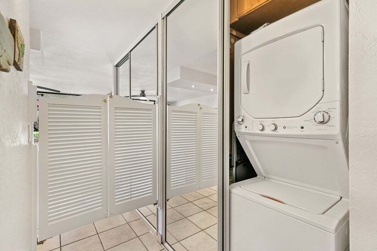 A laundry room with a front-loading washer and dryer, a tiled floor, and a white door with louvered panels.