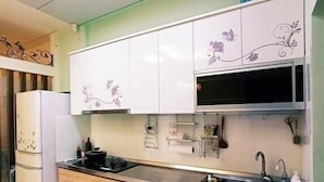 A kitchen with white cabinets, a stainless steel sink, and a microwave. - Tongxinyu Homestay (Wujie)