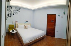 A bedroom with a bed, a green armchair, a small table, a wooden door, and a wall with a floral mural. - Tongxinyu Homestay (Wujie)