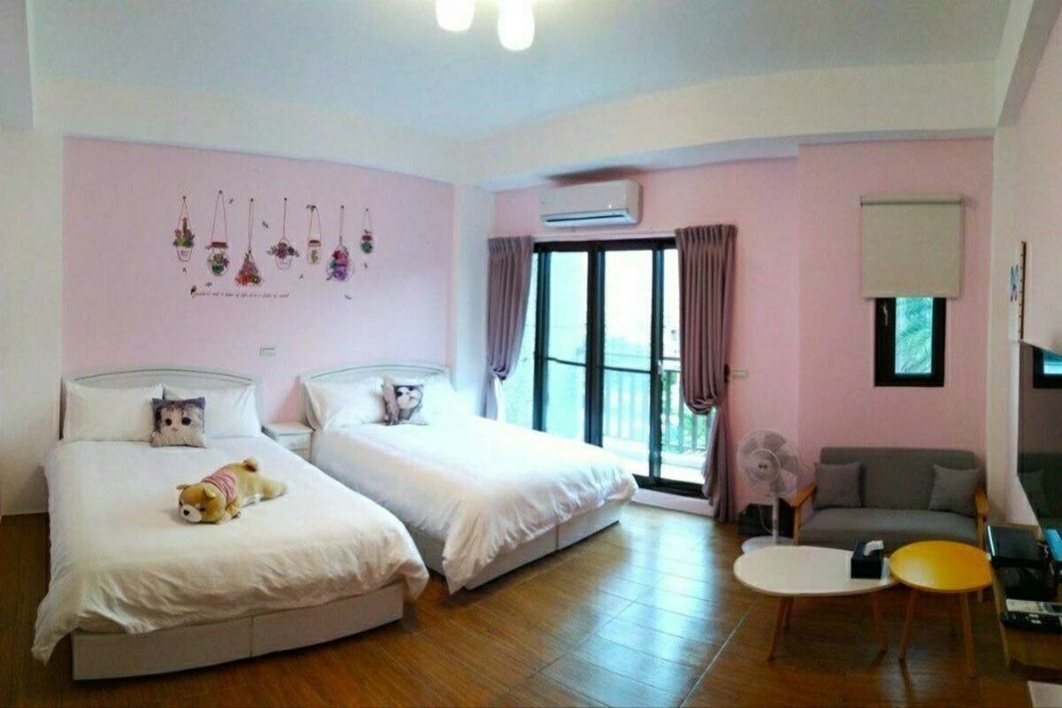 A room with two beds, a sofa, a small table, and a fan.