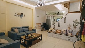 A modern living room with a sofa, coffee table, and decorative pillows. There is a staircase leading to an upper level, and a small table with plush toys. - Tongxinyu Homestay (Wujie)