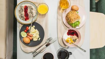 Ein Frühstücksbrett mit Rührei, Würstchen, einer Tomate und einer Scheibe Brot mit Butter und Marmelade.