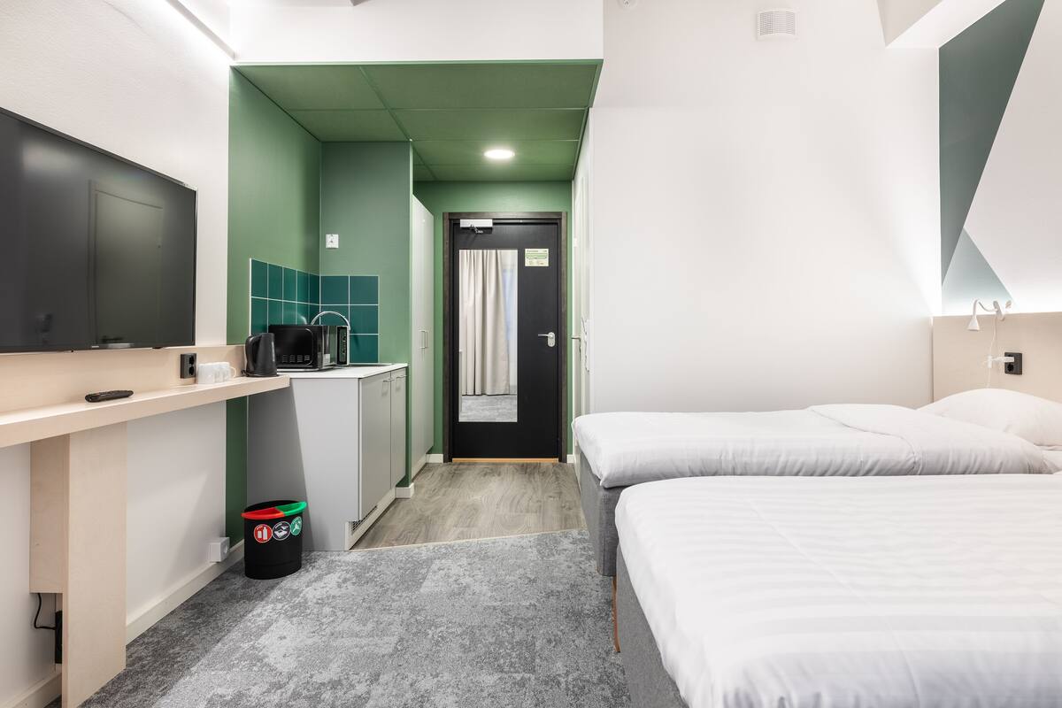 A hotel room with a bed, a desk with a computer, a small kitchenette, and a bathroom with a shower.